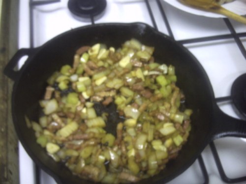 A cast-iron skillet with the bacon and vegetables cooking